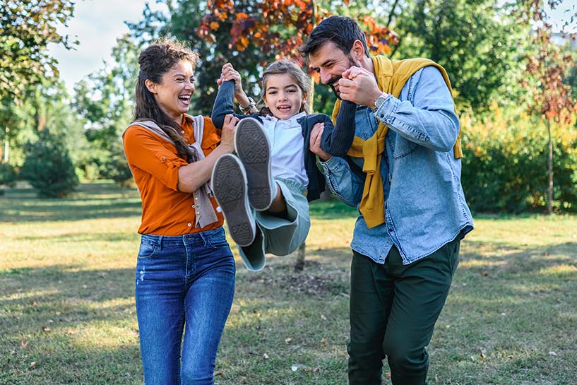 Two adults push a child on a swing.