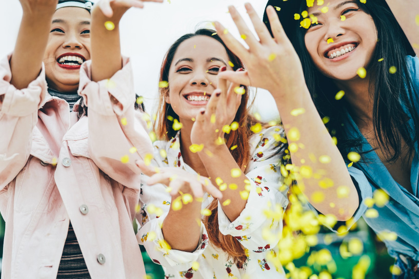 Women smile and toss flower petals into the air.