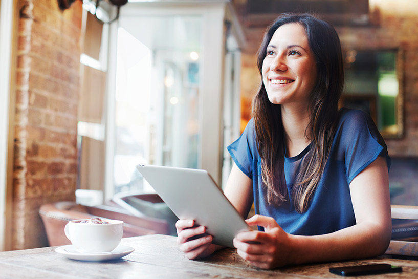 A woman in a coffee shop smiles as she uses her tablet device.