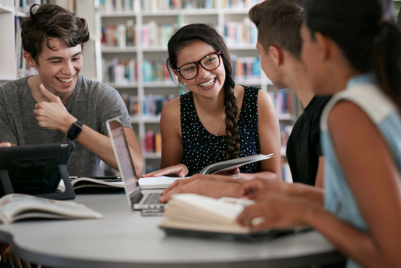 Students sit around a library table smiling.